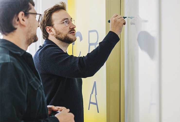 Two Angelbird colleagues collaborating at a whiteboard, with one writing ideas while the other observes attentively.