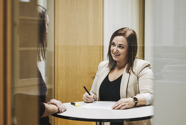 Angelbird collaborator standing at a table, signing or writing on a document while engaged in conversation with a colleague.