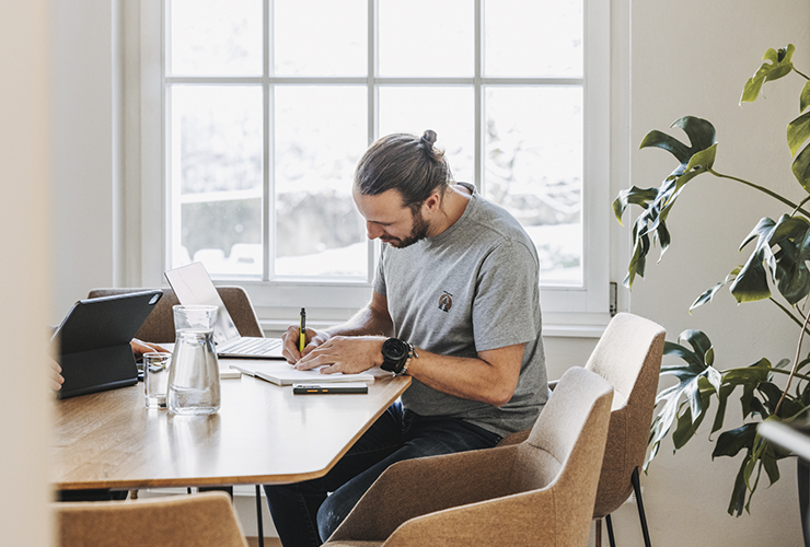 A man seated at a table, sketching ideas on paper in a creative workspace.