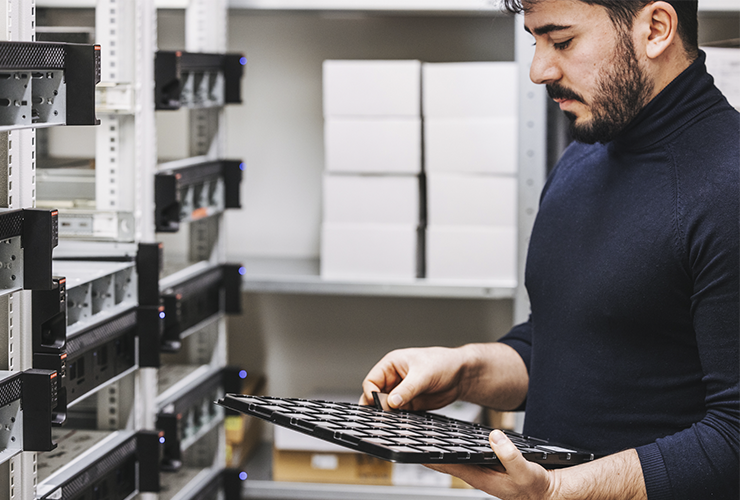 A man holding a tray with memory cards, positioned in front of a machine in a technical workspace.